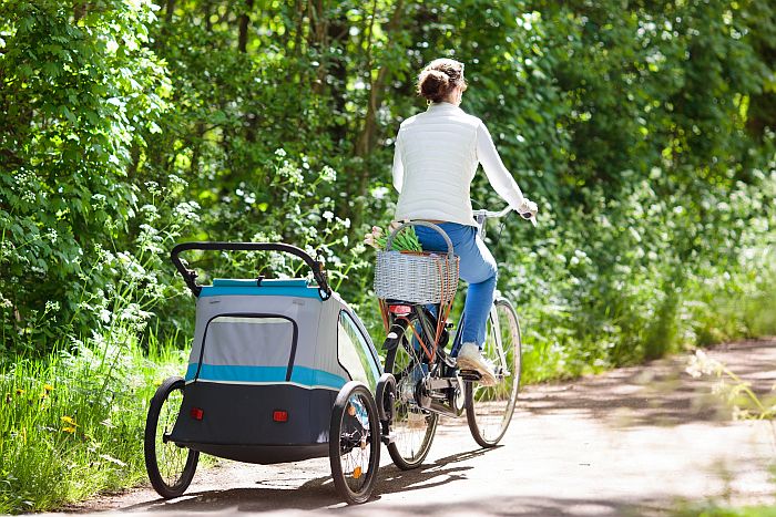 Mother on bicycle with baby bike trailer in park HTHIC Heritage & Slow TourismLAB by Elgin & Co. Image of woman cycling